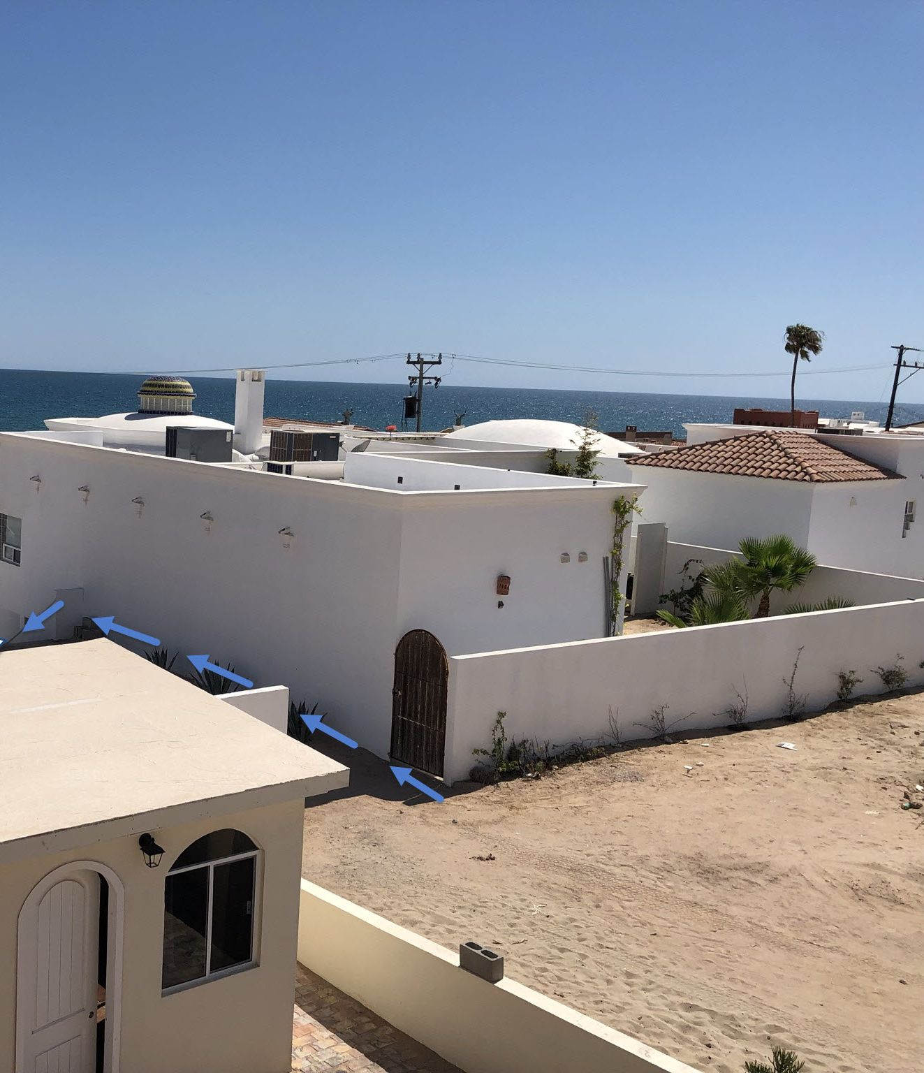 A residential area with white buildings, a clear blue sky, and a view of the sea.
