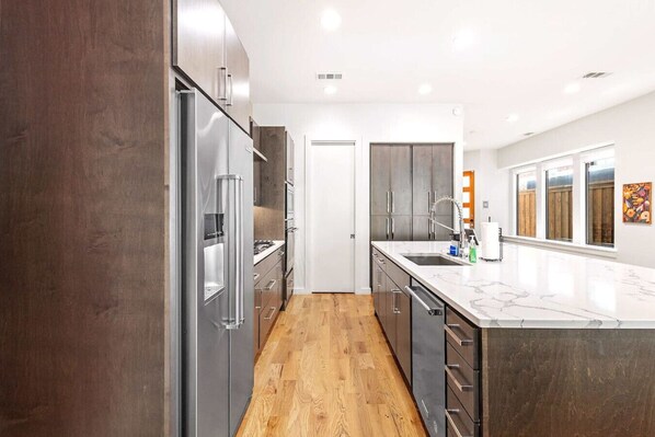 A modern kitchen with stainless steel appliances, a marble countertop, and wooden flooring.