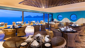 Un restaurant doté de chaises et de tables en osier, aménagé pour accueillir les convives, et offrant une vue panoramique sur la mer et les montagnes.