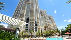 Un hotel moderno de gran altura con varios balcones, una piscina y palmeras a su alrededor.