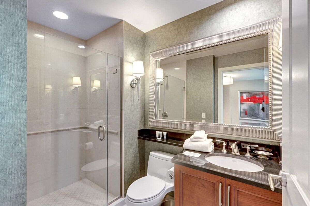 Une salle de bain moderne avec une douche à parois de verre, des toilettes blanches et un meuble-lavabo doté d’un grand miroir et de deux vasques.