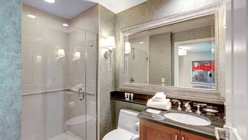 Une salle de bain moderne avec une douche à parois de verre, des toilettes blanches et un meuble-lavabo doté d’un grand miroir et de deux vasques.