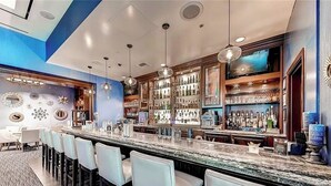 Zona de bar con una barra alargada, varias luces colgantes y una variedad de botellas en estanterías.