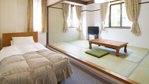 Ein traditioneller japanischer Raum mit Tatami-Boden, einem Bett mit Holz-Kopfstück, einem kleinen Tisch und einem Fernseher.