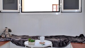 A room with a window, a small table with a cup and a plant, and a plush toy on a shelf.