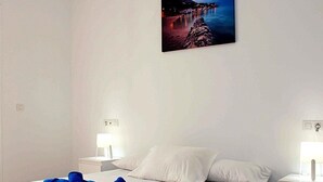 A hotel room with a large bed, white bedding, two bedside lamps, and a wall-mounted picture of a coastal scene.