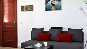 A living room with a grey sofa, two red cushions, a small black table with a white mug and a blue cup, and a framed picture on the wall.