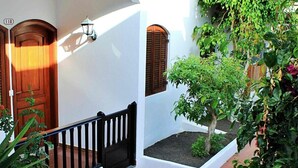 Um pátio com um edifício branco, portas de madeira, grades pretas e plantas verdes.