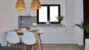 Uma cozinha moderna com armários brancos, uma mesa de jantar com cadeiras e duas luminárias de vime suspensas.