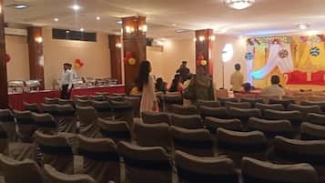 A banquet hall with rows of chairs, a stage with draped curtains, and a buffet table.