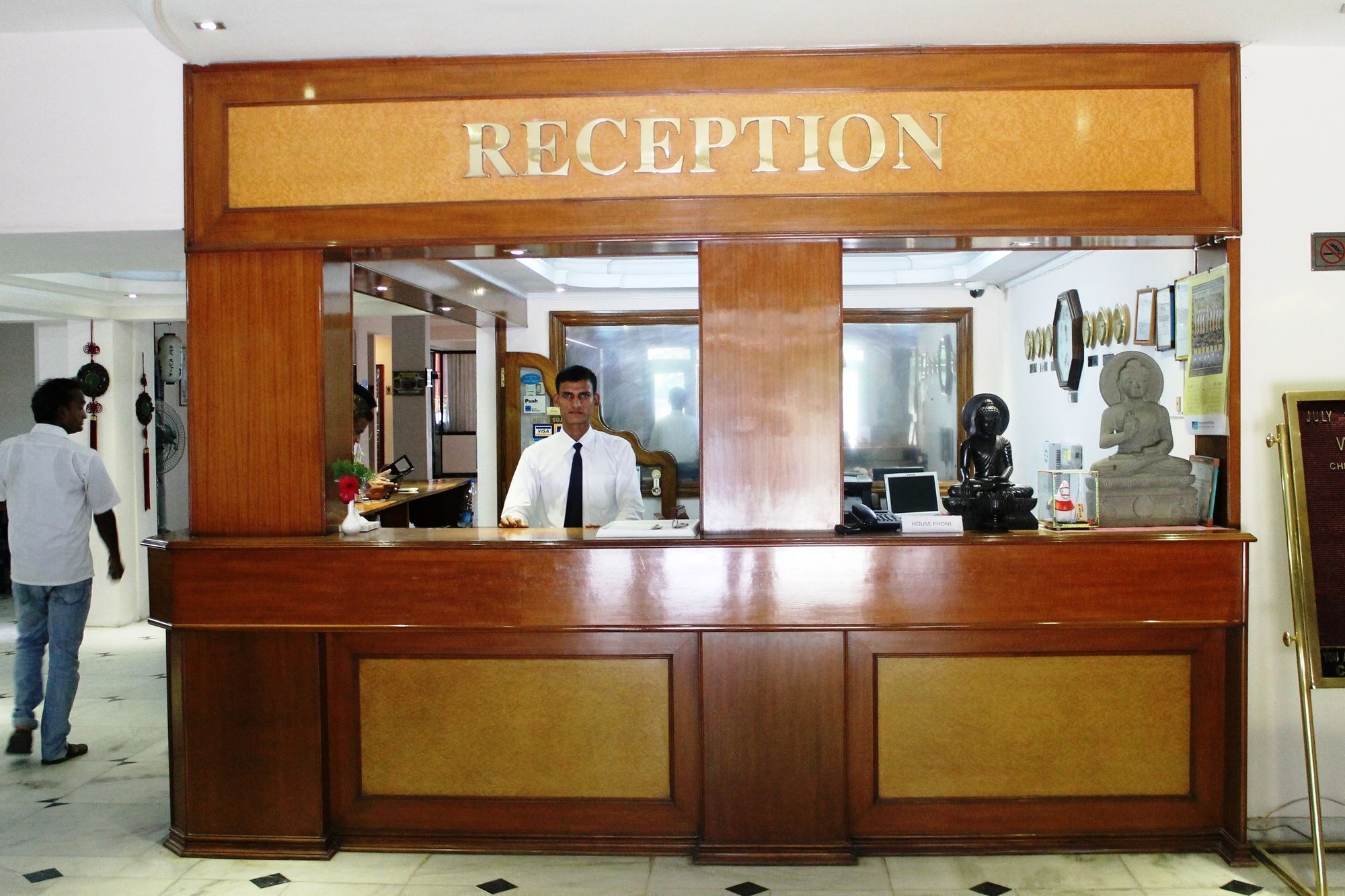 A reception desk with a 'RECEPTION' sign, a man standing behind it, and a statue on the right.