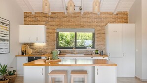 Une cuisine moderne avec des meubles blancs, un îlot central en bois et un mur en briques.