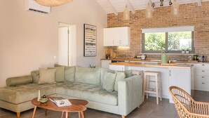 Un salon moderne avec un canapé vert, une table basse en bois et une cuisine dotée de meubles blancs et d’un mur en briques.