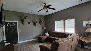 A spacious living room with a sectional sofa, a ceiling fan, and mounted deer heads on the wall.
