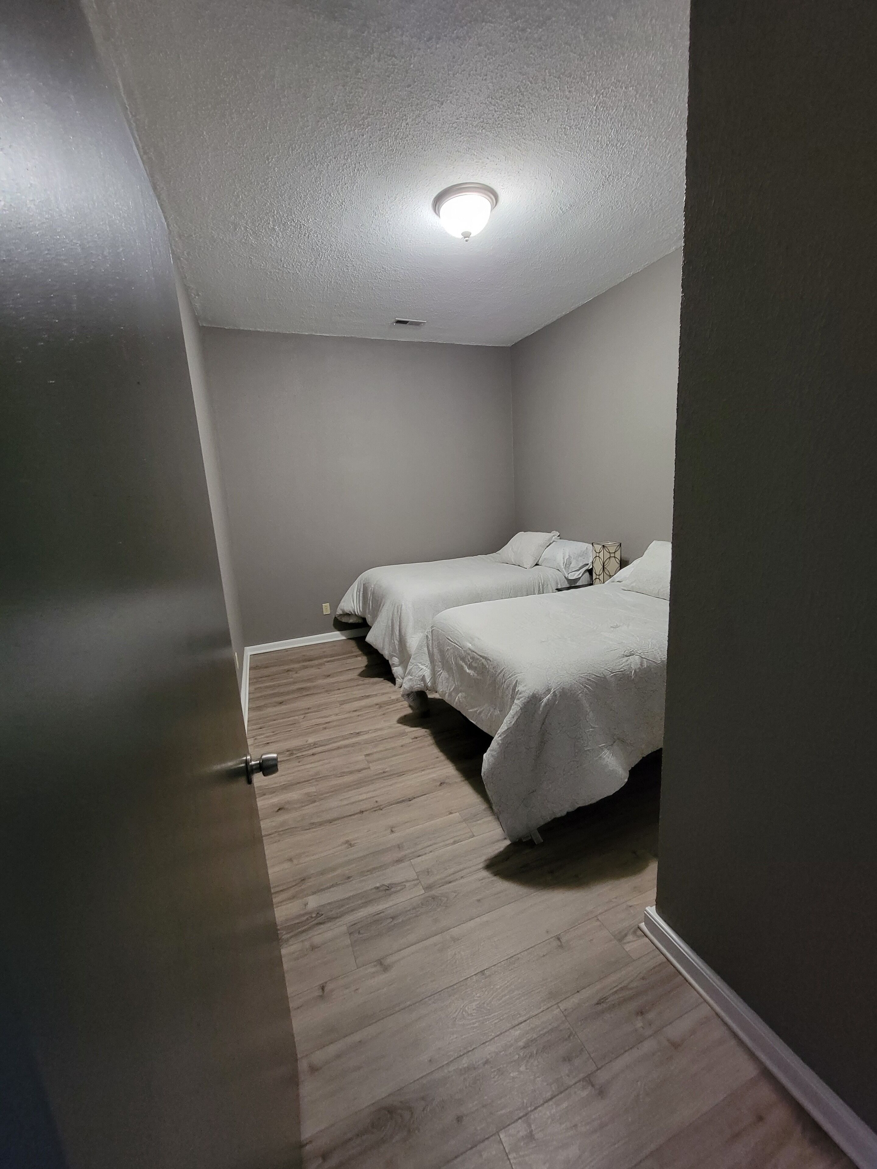 A bedroom with two beds, a wooden floor, and a white ceiling light.
