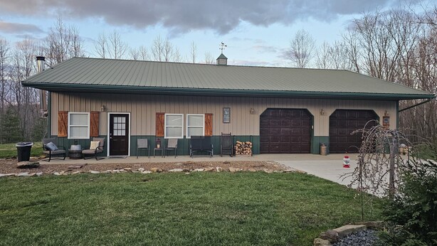 A building with a green and beige exterior, a front porch with chairs and a fire pit, and two large garage doors.