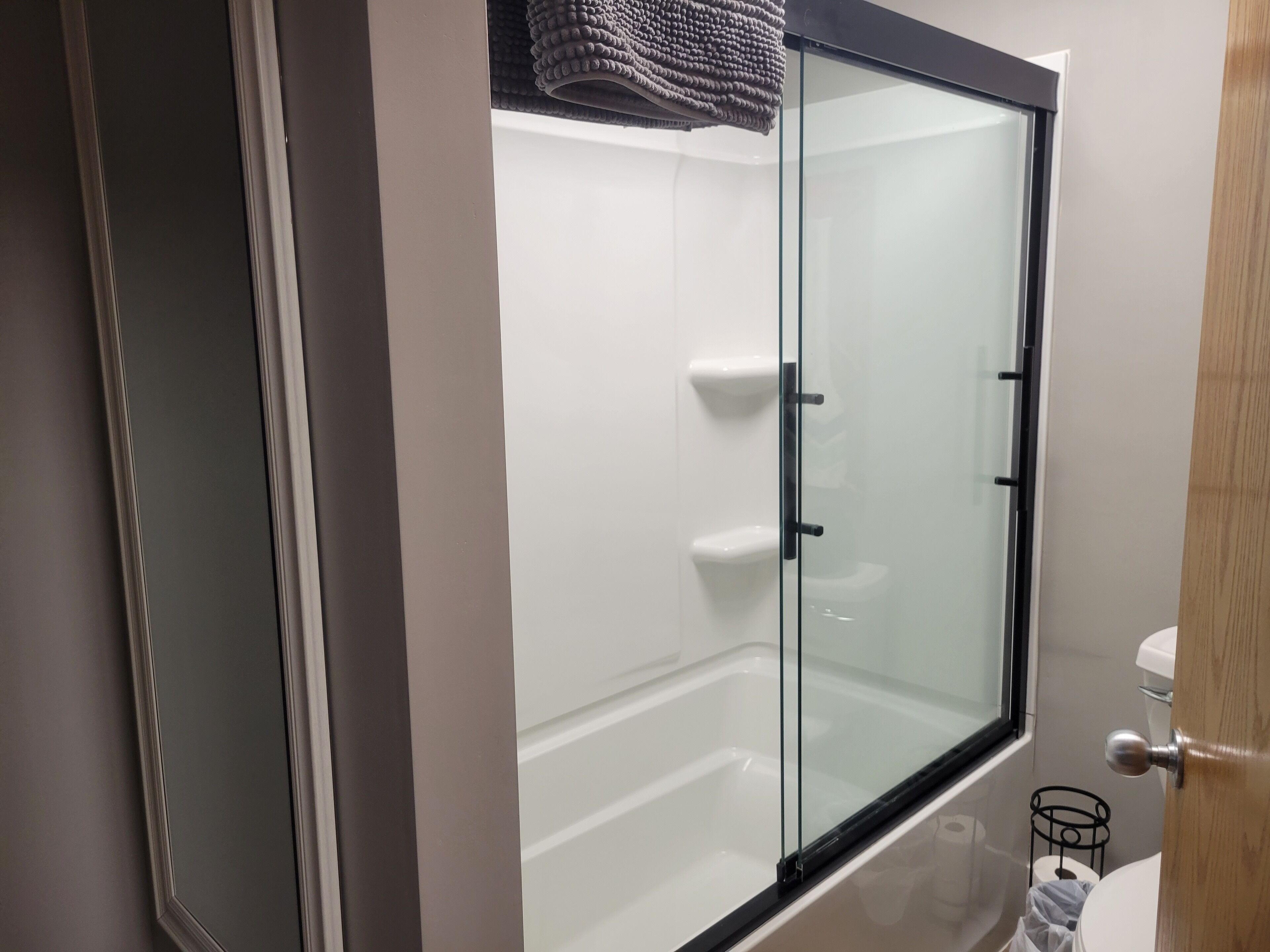 A modern bathroom with a glass shower enclosure, a white toilet, and a small trash bin.