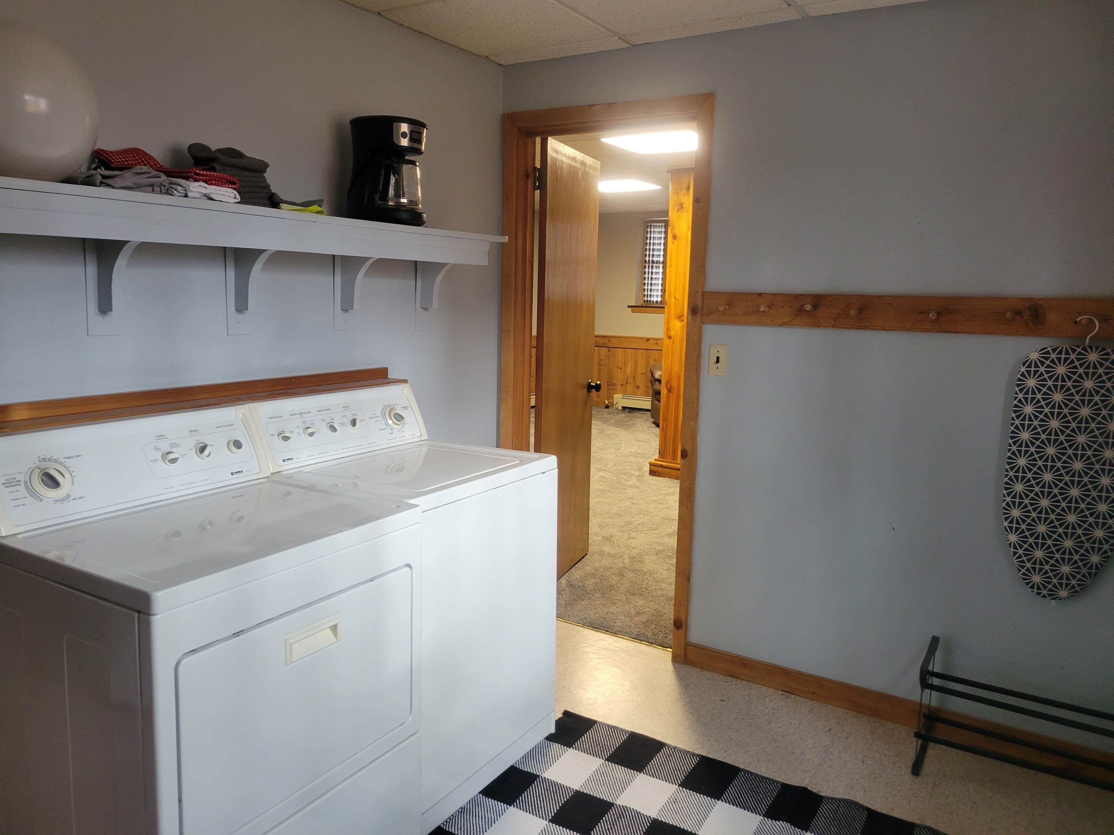 A laundry room with a washer and dryer, a coffee maker on a shelf, and a patterned rug on the floor.