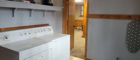 A laundry room with a washer and dryer, a coffee maker on a shelf, and a patterned rug on the floor.
