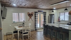 A kitchen with a wooden ceiling, a dining area with white chairs, a bar area with stools, and a sign indicating 'Abbey Road'. - Walking distance to four-season ski and golf resort Crystal Mountain (Thompsonville)