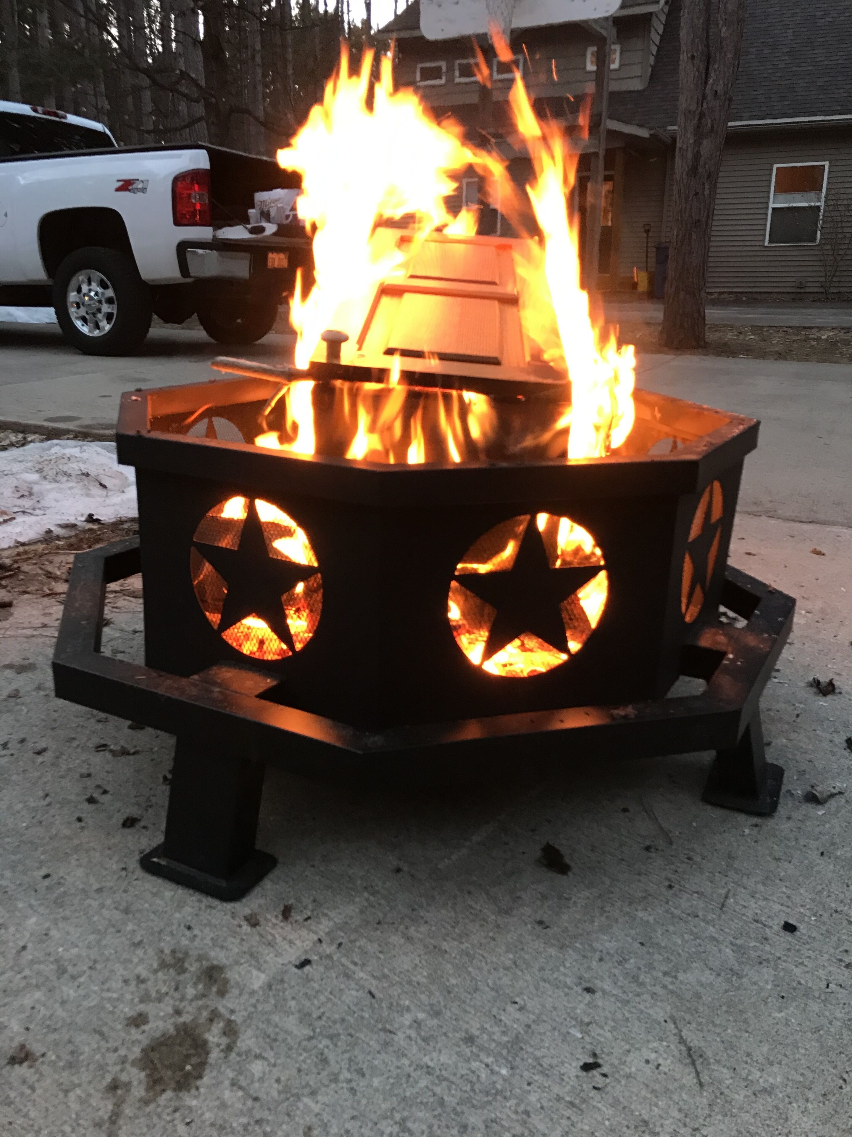 A metal fire pit with star-shaped openings, placed on a concrete surface outdoors.
