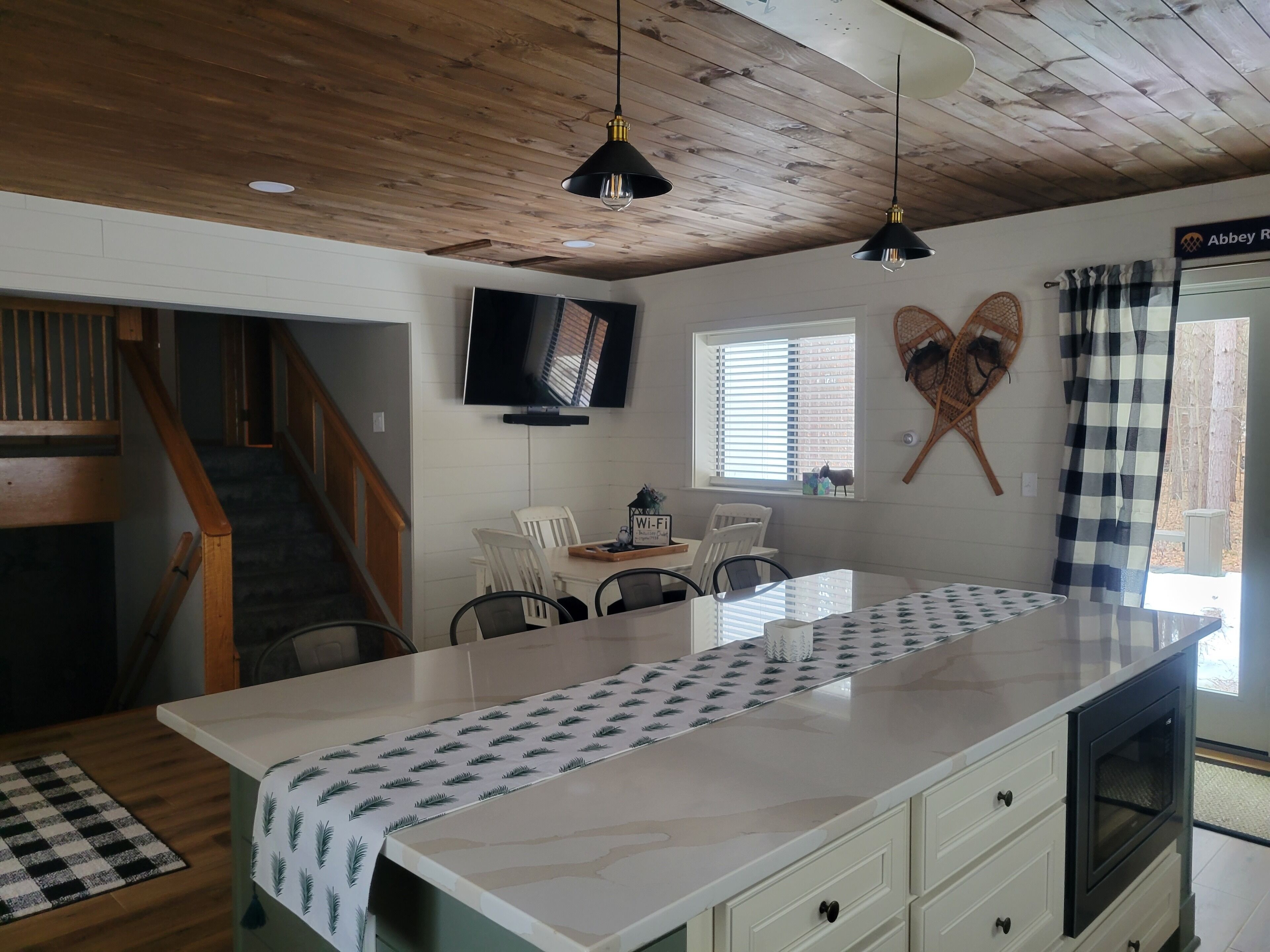 Una cocina moderna con una isla central, techo de madera y un comedor con sillas blancas y una mesa.