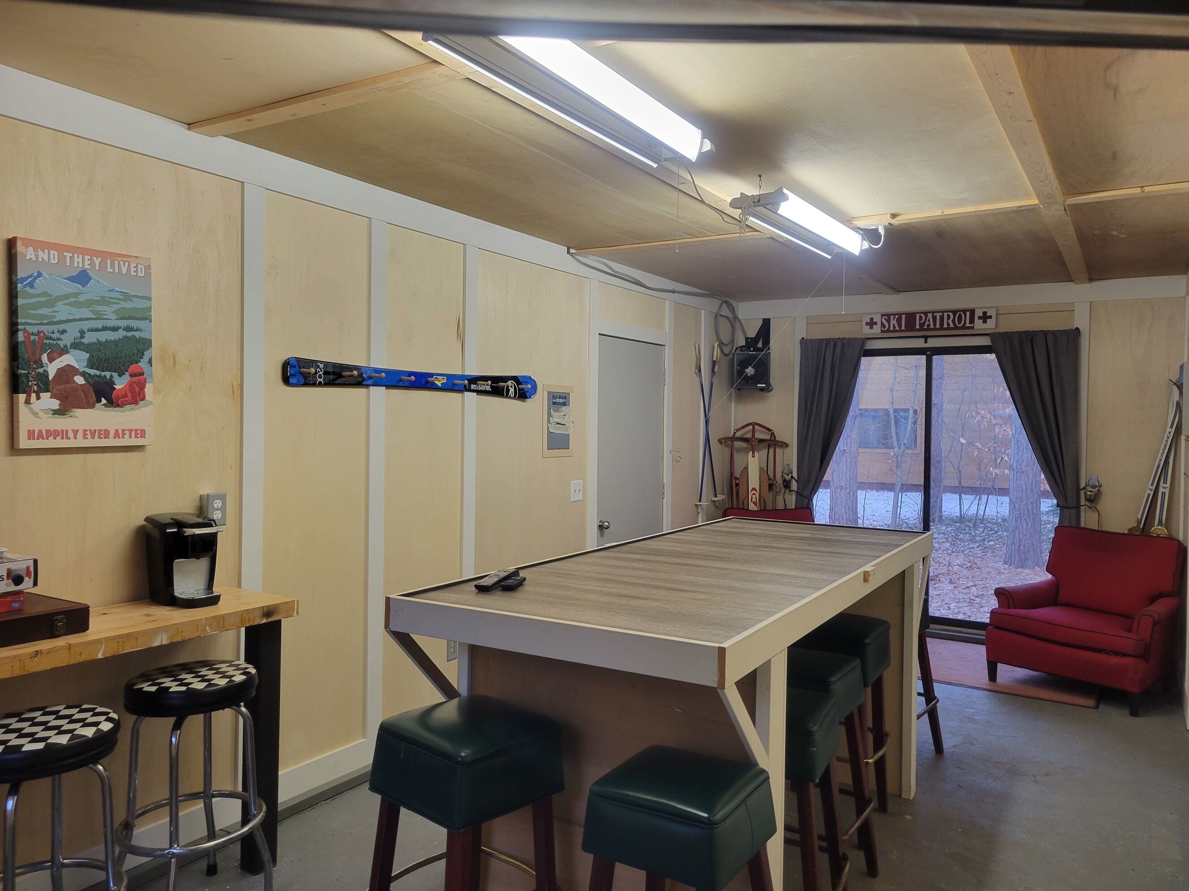 A room with a wooden ceiling, a bar area with stools, a red chair, and a ski patrol sign.