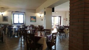 A restaurant with multiple tables and chairs, a tiled floor, and a brick wall. - Al Poggio dei Papi (Citta della Pieve)