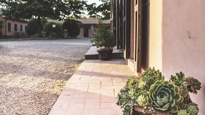 A building with a gravel courtyard, a potted succulent plant, and a tiled pathway. - Al Poggio dei Papi (Citta della Pieve)