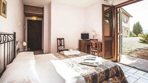 A bedroom with a bed, a desk with a computer, a chair, and a door leading to an outdoor area. - Al Poggio dei Papi (Citta della Pieve)