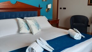 A neatly made bed with white linens and blue accents, a wooden headboard, and a painting above. - Hotel D Apos Angelo Palace (Mazara del Vallo)