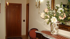A room with a wooden door, a chair, a table with a vase of flowers, and a mirror. - Hotel D Apos Angelo Palace (Mazara del Vallo)