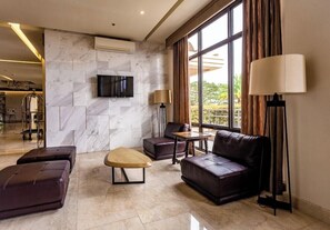 A modern living room with a marble wall, leather furniture, a flat-screen TV, and large windows with curtains.