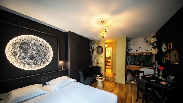 A hotel room with a bed, a round wall decoration, a dining table, and a kitchen area. - Studio Nature Avec vue sur le Château (Caen)