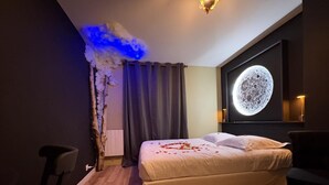 A modern bedroom with a bed, a wall-mounted circular light, and a tree branch decoration. - Studio Nature Avec vue sur le Château (Caen)