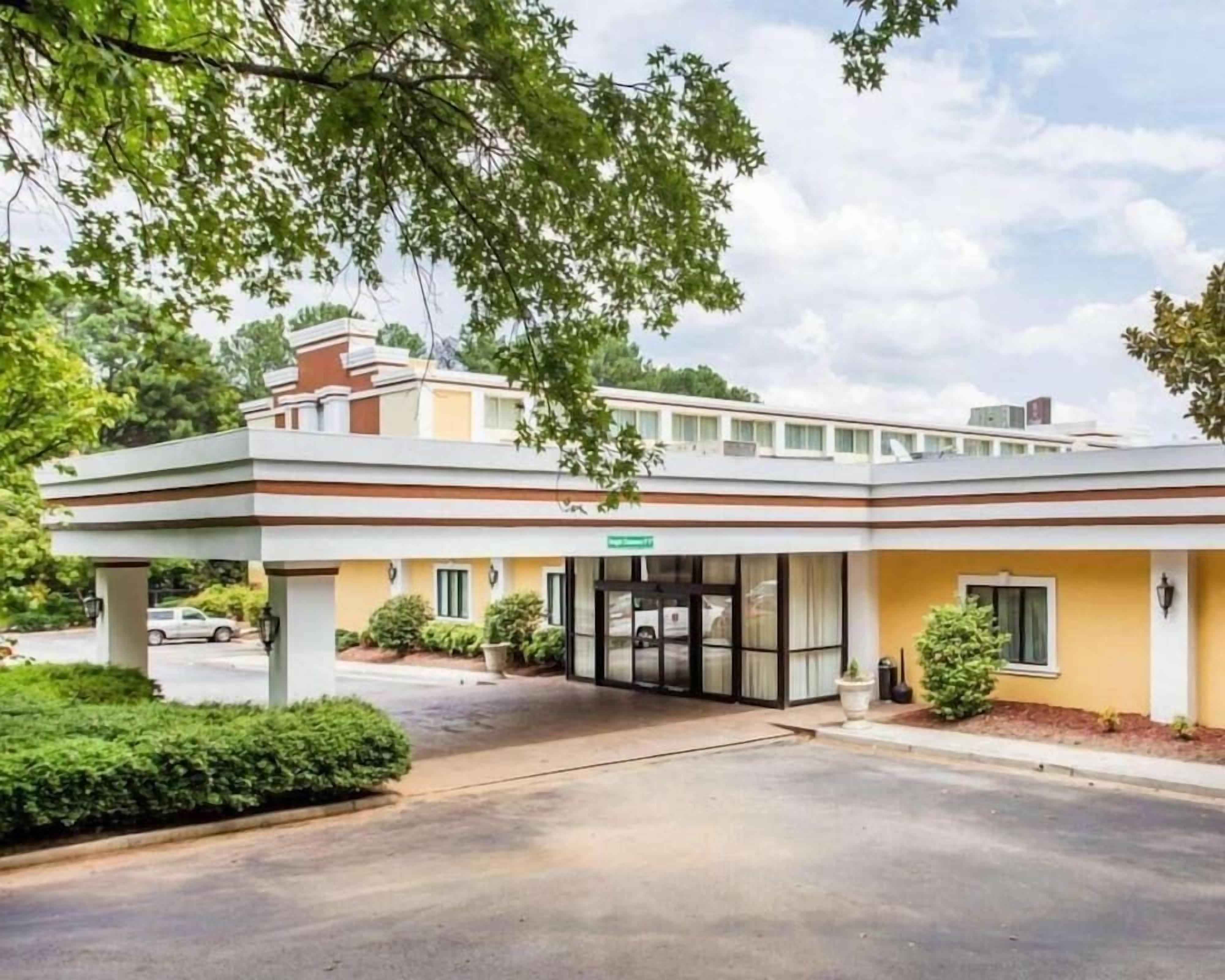 A hotel with a covered entrance, a parking lot, and a clear sky.