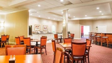 A hotel dining area with multiple tables and chairs, a kitchen area, and a whiteboard on the wall.