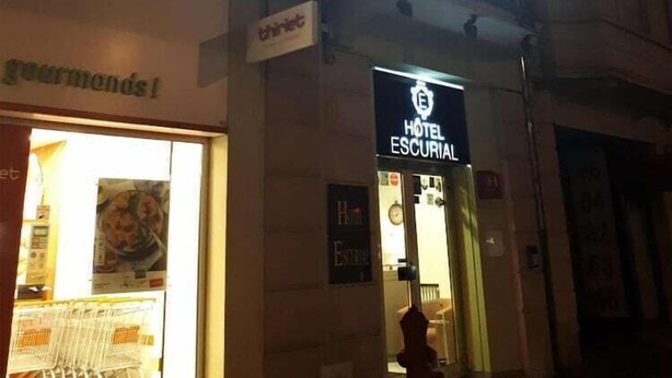 Un hotel llamado "HOTEL ESCURIAL" con un letrero luminoso, una entrada visible y un hidrante en el exterior.