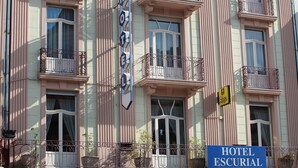 Un hotel de varios pisos con balcones, un cartel que indica 'HOTEL ESCURIAL' y un letrero de 'Logis'.