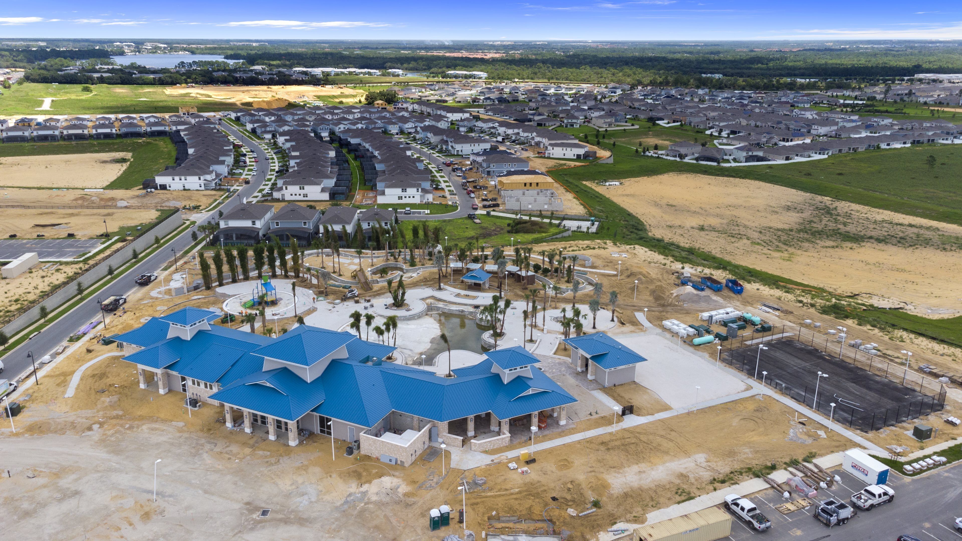 Zona residencial con casas modernas, un edificio comunitario central con techos azules y un amplio espacio abierto con construcción en curso.