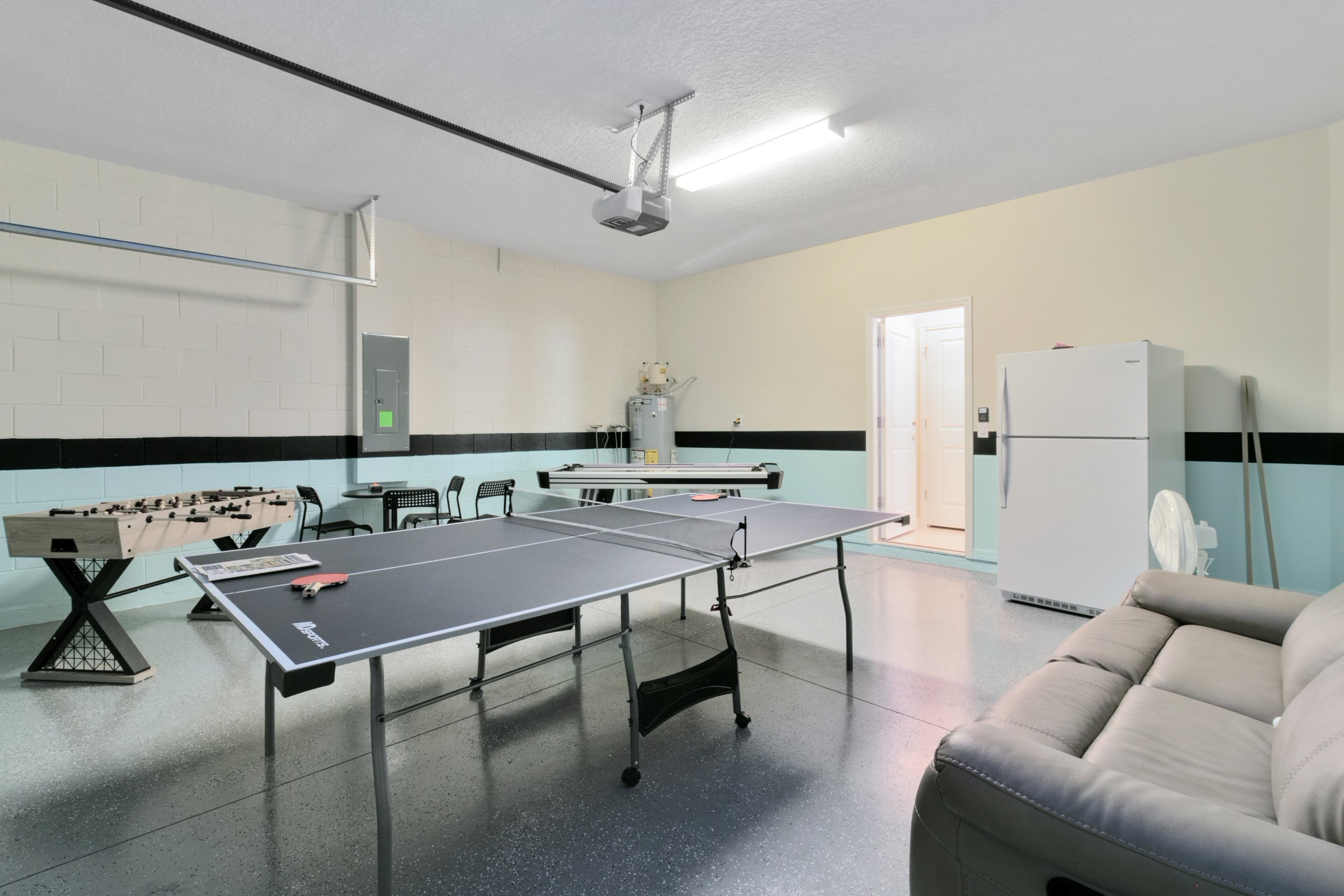 A room with a ping pong table, foosball table, and a sofa.