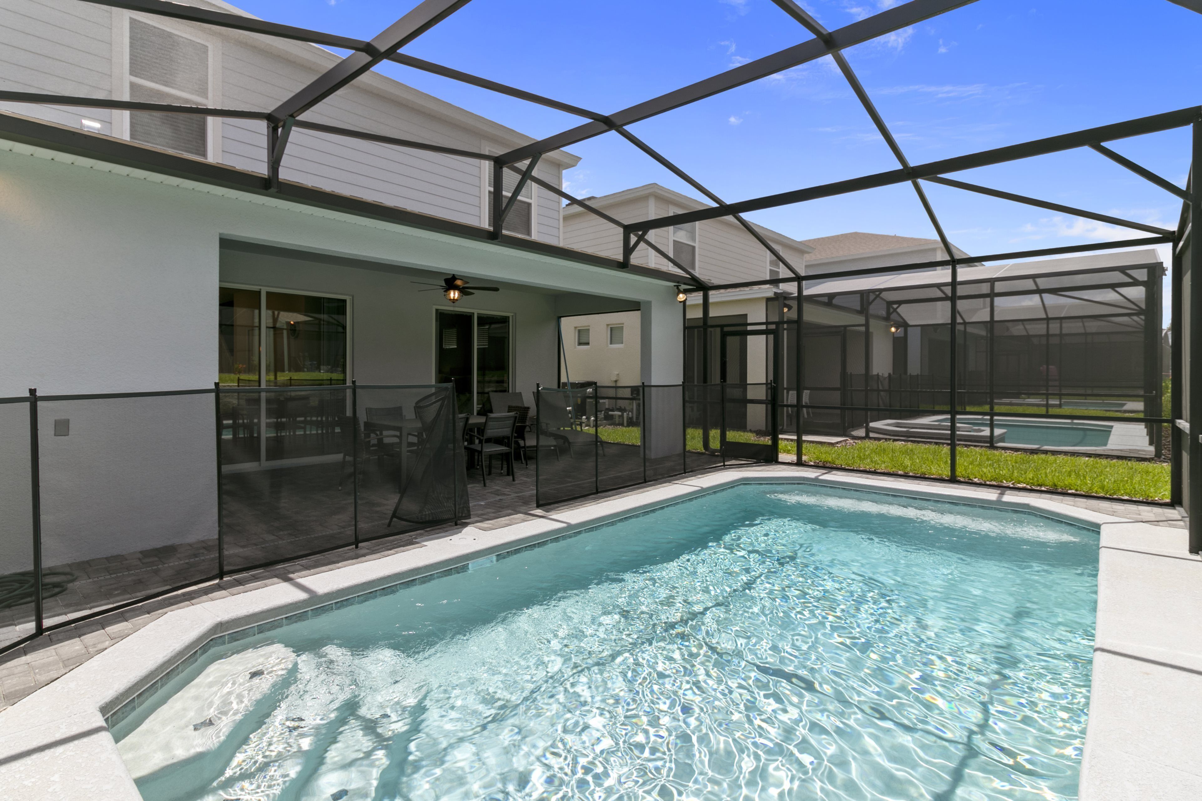 A swimming pool with a glass enclosure, surrounded by a covered patio area with outdoor furniture.