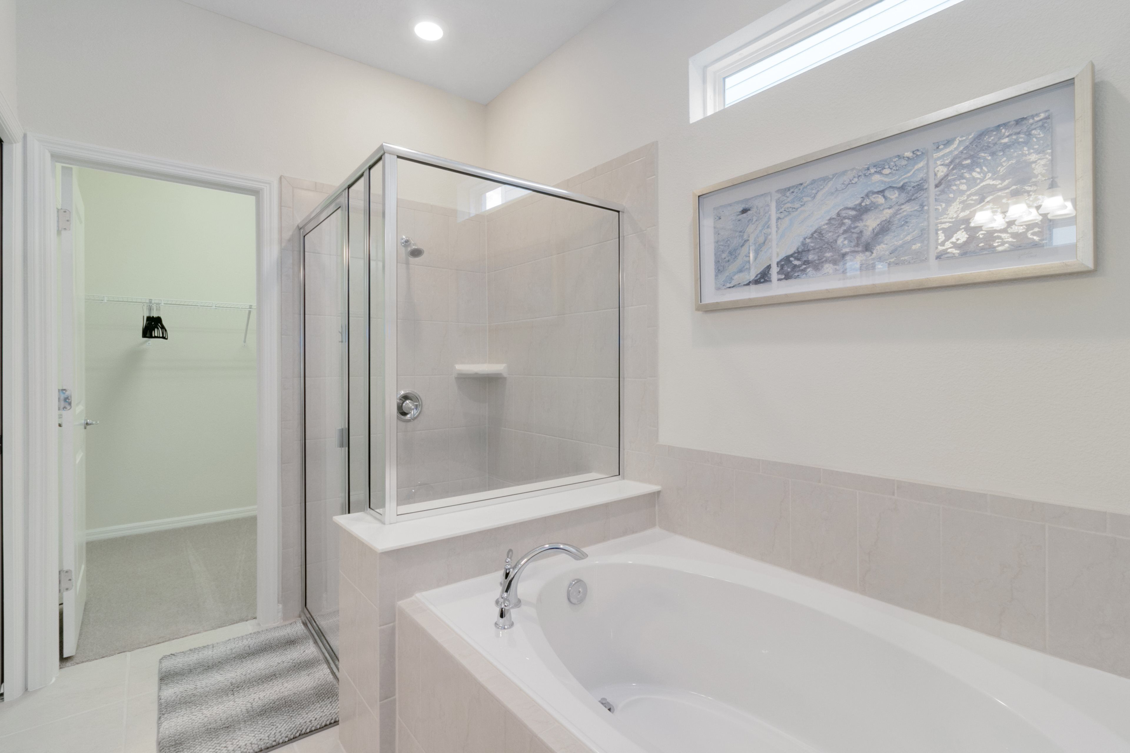 A modern bathroom with a glass-enclosed shower, a freestanding bathtub, and a framed artwork on the wall.