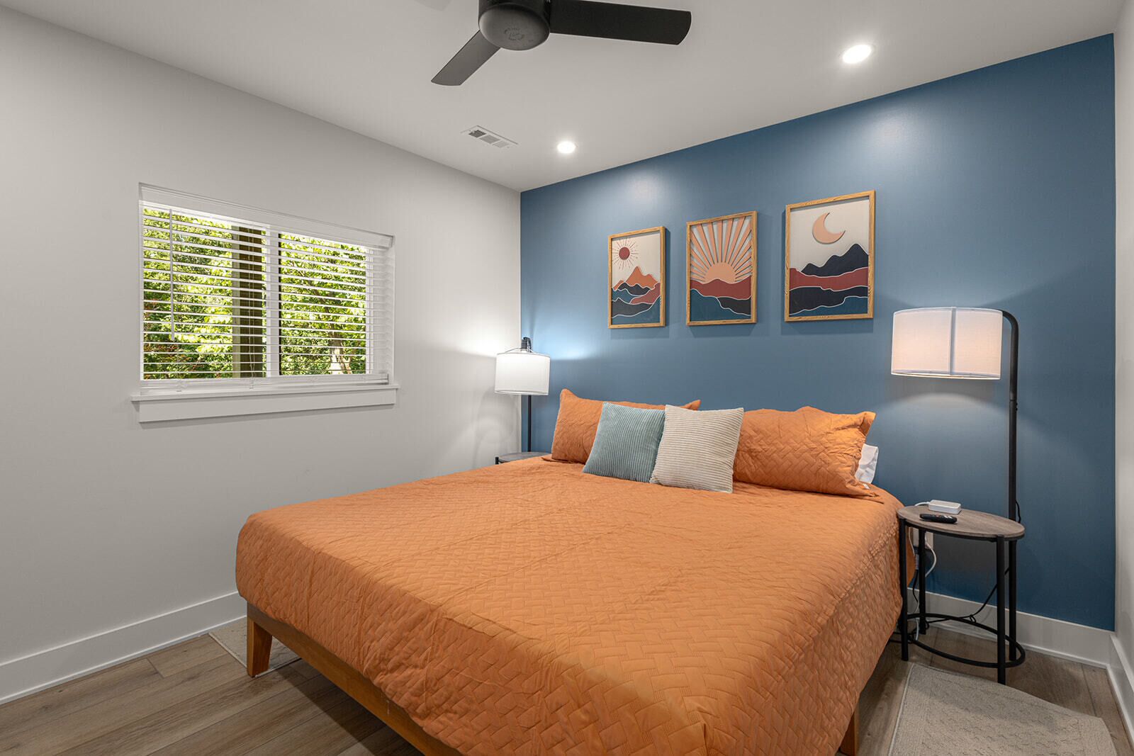 Une chambre à coucher avec un lit, une fenêtre avec des stores, un ventilateur de plafond et des œuvres d’art murales.