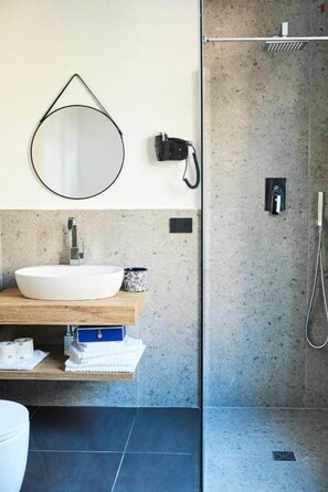 A bathroom with a round mirror, a white sink, a towel rack, and a shower area. - Central Lodge (Rome)