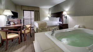 Habitación de hotel con cama, escritorio con silla, lámpara de escritorio, televisor, ventana con cortinas, lámpara de pared y bañera.