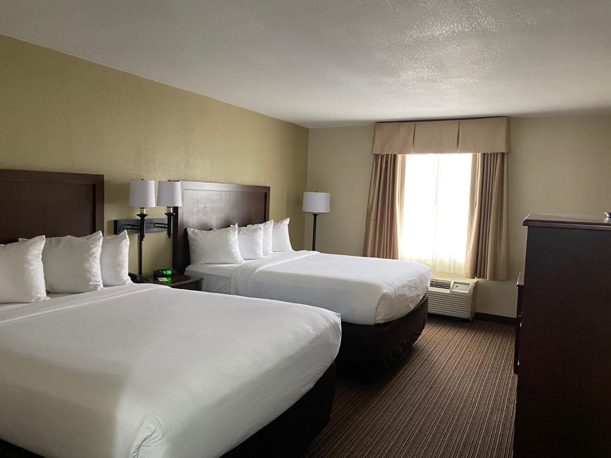 A hotel room with two beds, a desk, a lamp, and a window with curtains.