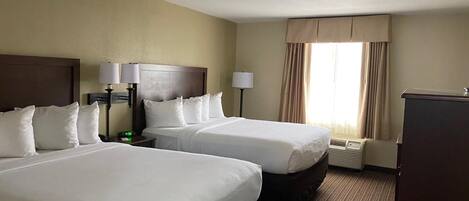 A hotel room with two beds, a desk, a lamp, and a window with curtains.