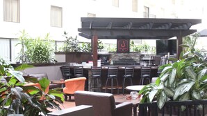 Zona de bar al aire libre con varias opciones de asientos, una barra y una pantalla de televisión.