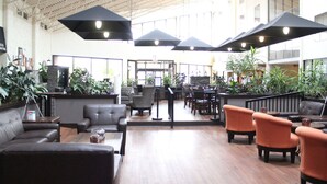 Amplio espacio interior con diversos arreglos de asientos, incluyendo sofás y sillones, y una variedad de plantas en macetas.